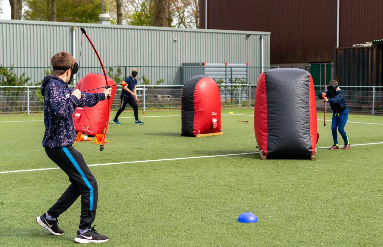 Kinderen schuilen achter obstakels tijdens archery tag op een sportveld