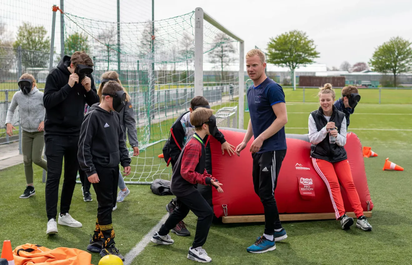 Zes kinderen en drie volwassenen spelen archery tag op een voetbalveld