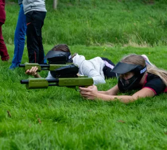 Twee kinderen liggen op een grasveld met twee paintball geweren voor kinderen