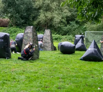 Drie kinderen zitten verscholen achter camouflage obstakels tijdens een paintball spelvorm