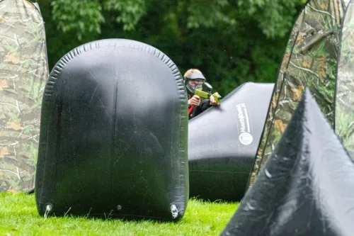 Een speler richt zijn paintball geweer tussen meerdere obstakels op een grasveld