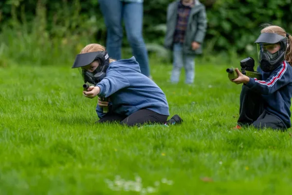 Twee spelers zitten met paintballguns en maskers op het gras