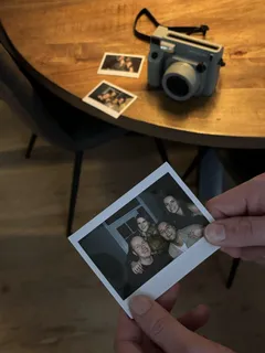 Polaroid foto in de hand met de Fujifilm Instax camera op tafel